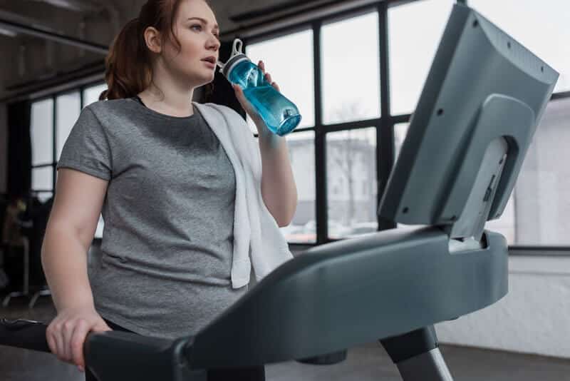 girl drinking water running treadmill gym