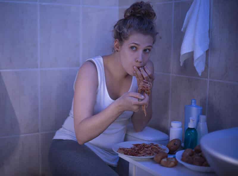 Girl stuffing herself with spaghetti in bathroom